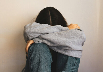 Eine Frau sitzt auf dem Boden, die Arme um den Kopf geschlungen