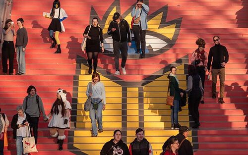 Menschen gehen die bunte Treppe der Leipziger Buchmesse hinunter; Bild: Leipziger Messe GmbH / Tom Schulze 