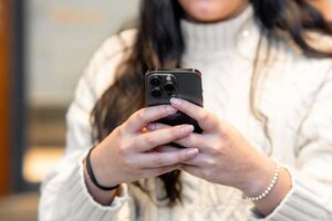 Eine Nahaufnahme einer Person, die ein Handy in der Hand hält; Bild: Julio Lopez auf Unsplash Frau in weißem Pullover hält ein schwarzes Smartphone in den Händen.