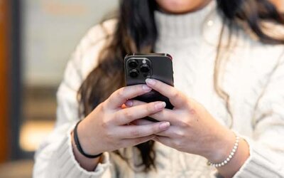 Frau in weißem Pullover hält ein schwarzes Smartphone in den Händen.