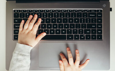 Kinderhände tippen auf einer Laptoptastatur.
