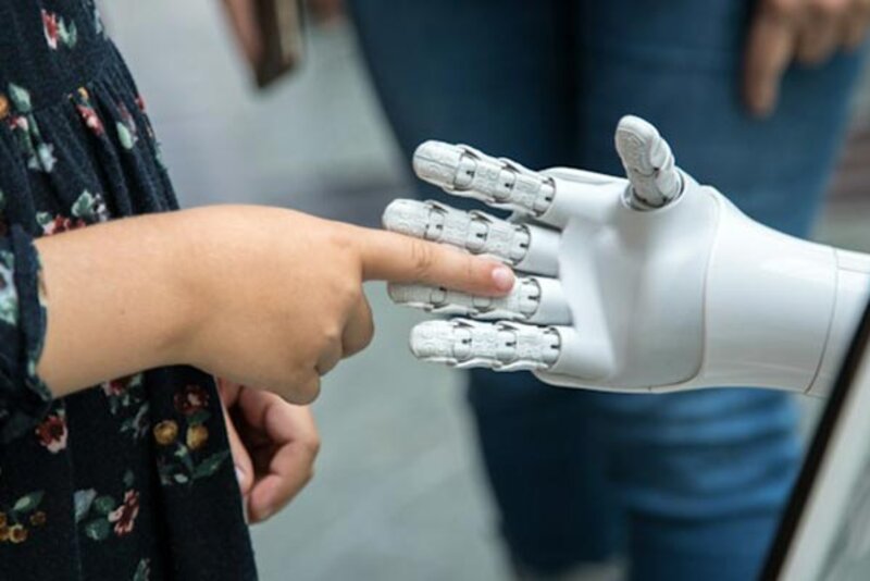 Kind berührt weiße Roboterhand; Bild: Katja Ano auf Unsplash