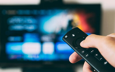 Eingeschalteter Flachbildfernseher mit Fernbedienung; Bild: Glenn Carstens-Peters auf Unsplash